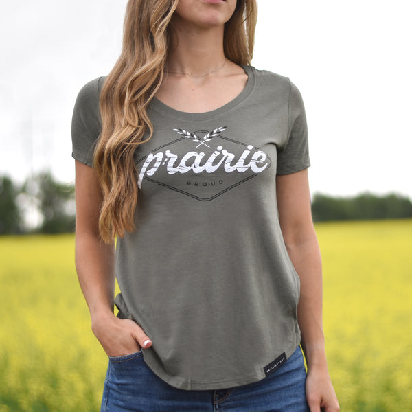 Woman wearing a greenish grey t-shirt with 'Prairie Proud' text in a field.