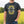 A man wearing a dark charcoal gray t-shirt with a floral yellow canola design and white 'Prairie Proud' graphic, standing in a blurred yellow canola field.