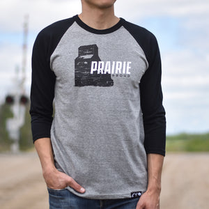 Person wearing a gray 3/4 sleeve shirt with black sleeves, the text 'Prairie Proud' and a grain elevator design.
