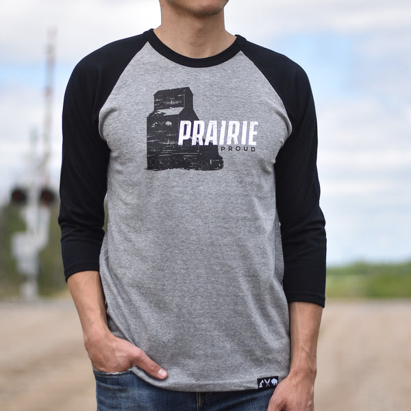 Person wearing a gray 3/4 sleeve shirt with black sleeves, the text 'Prairie Proud' and a grain elevator design.