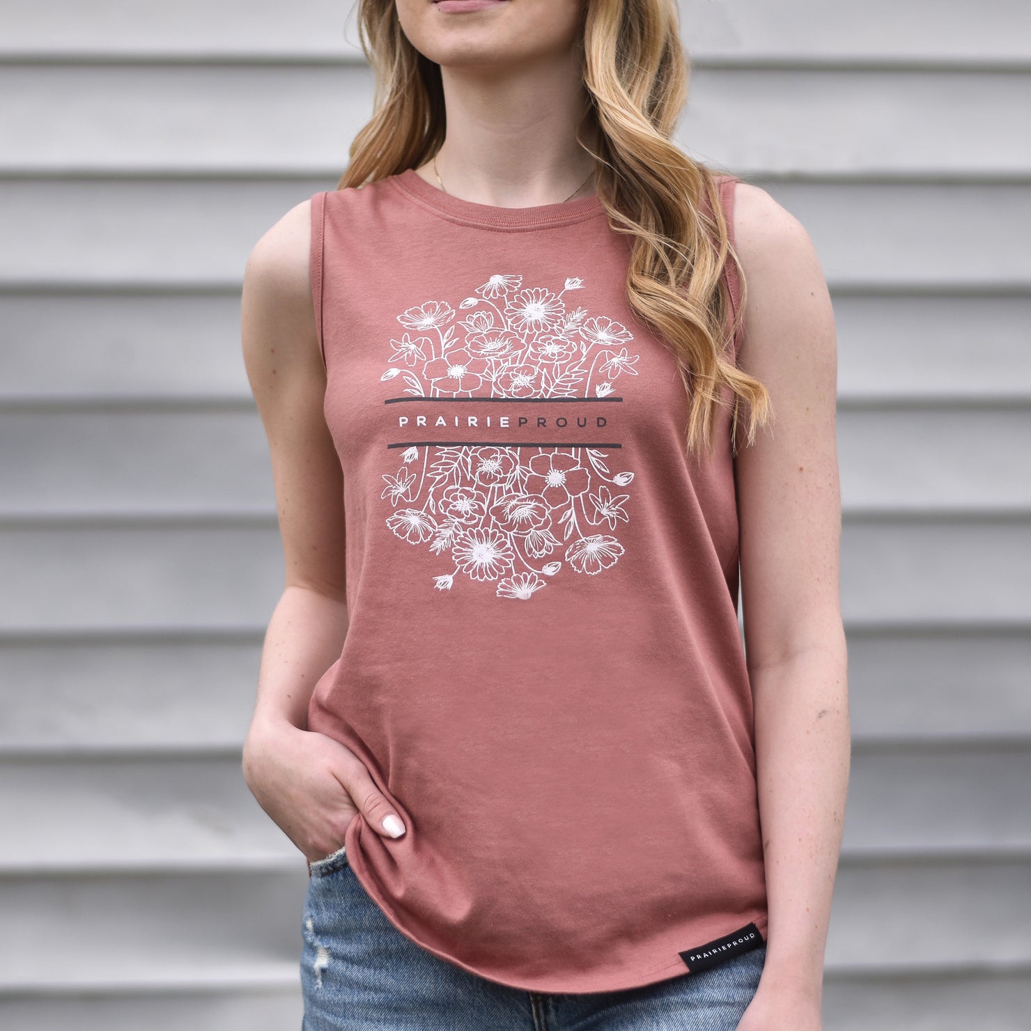 A woman wearing a sleeveless dusty rose tank top with a floral design and the text 'prairie proud'.