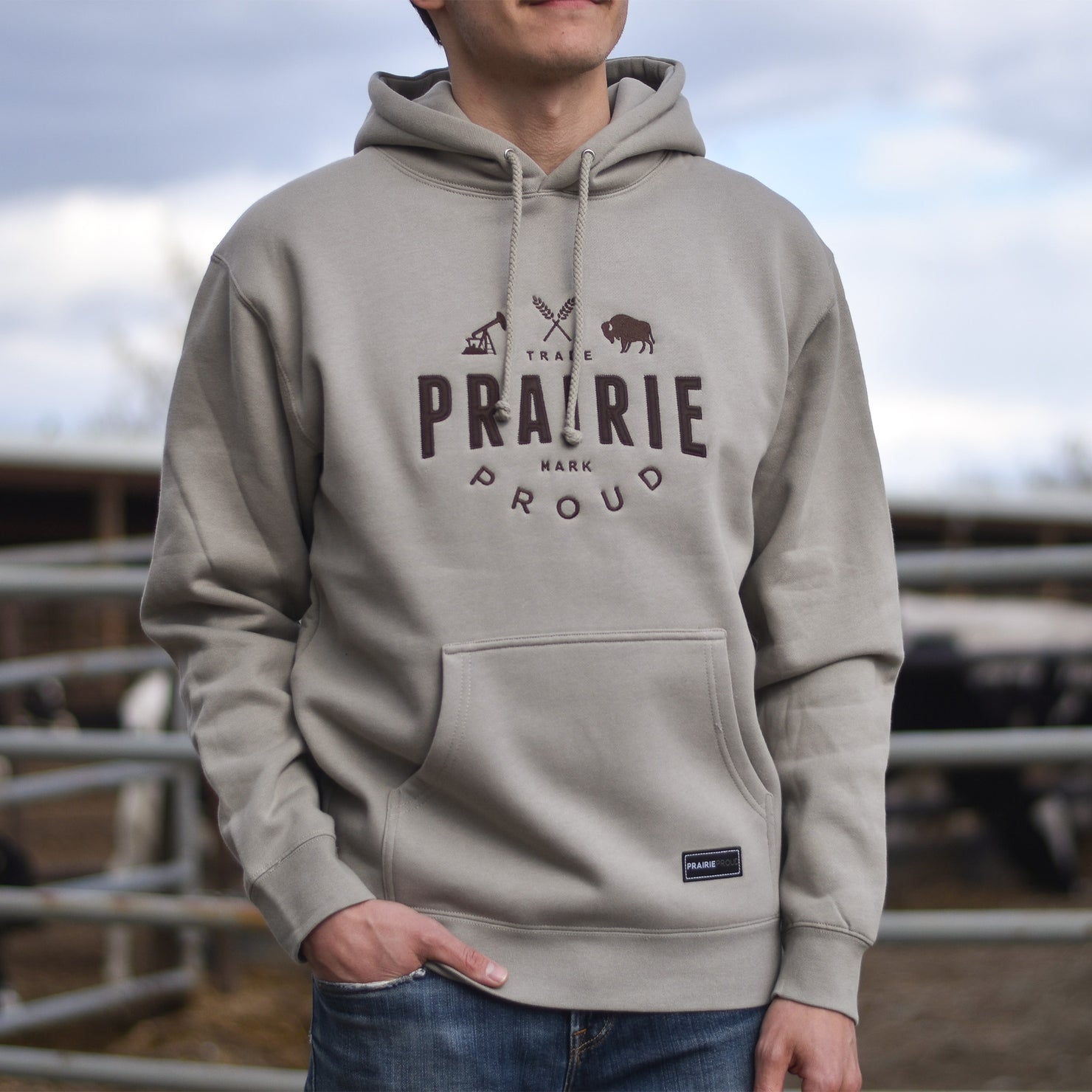 A person wearing a tan coloured hoodie with 'PRAIRIE PROUD' embroidered on the front.