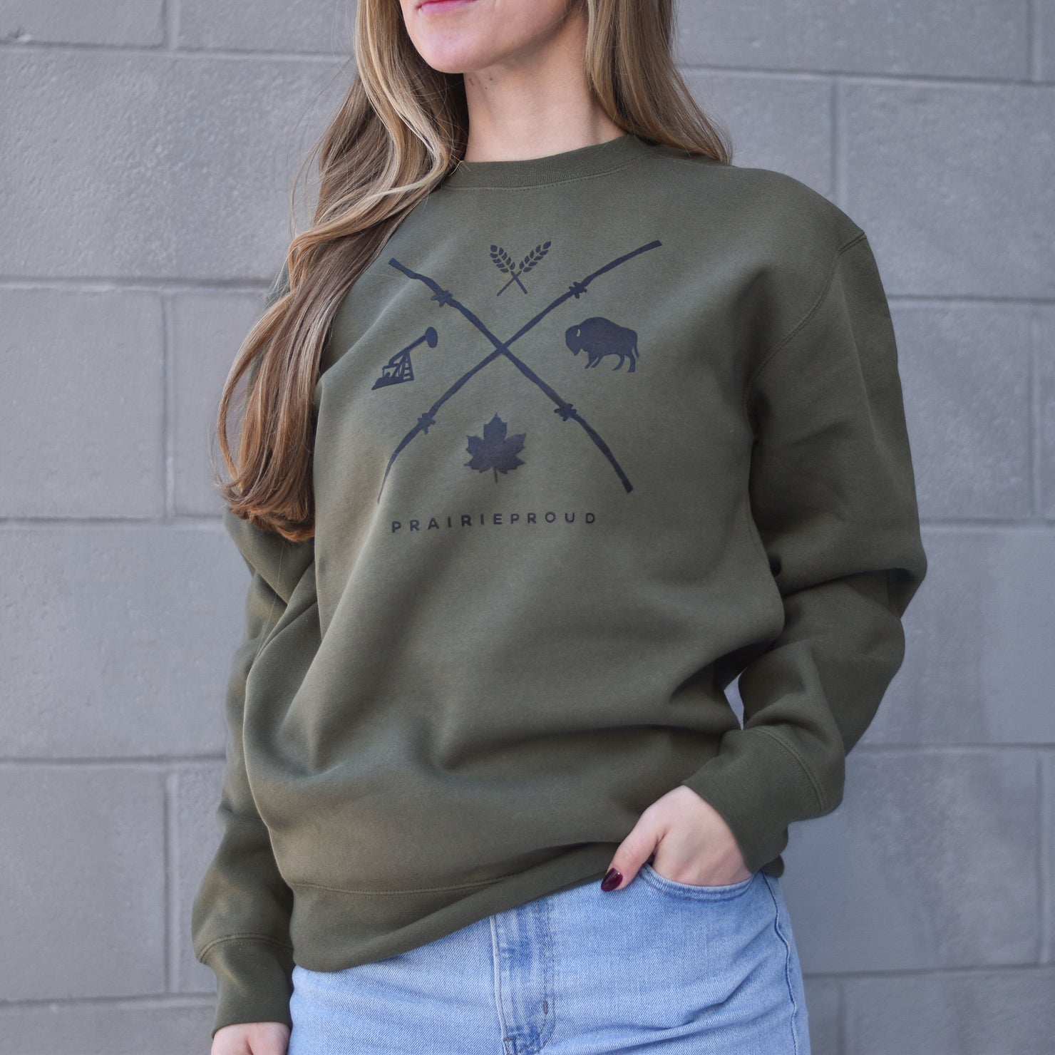 A person wearing an army green crew-neck sweater with a barbed wire design in the shape of an 'X'.